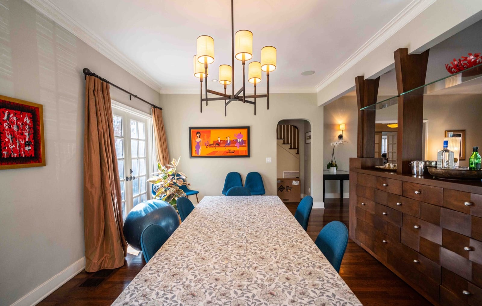 Dining room with a long stone-topped table, blue upholstered chairs, a multi-arm chandelier and French doors to the garden.